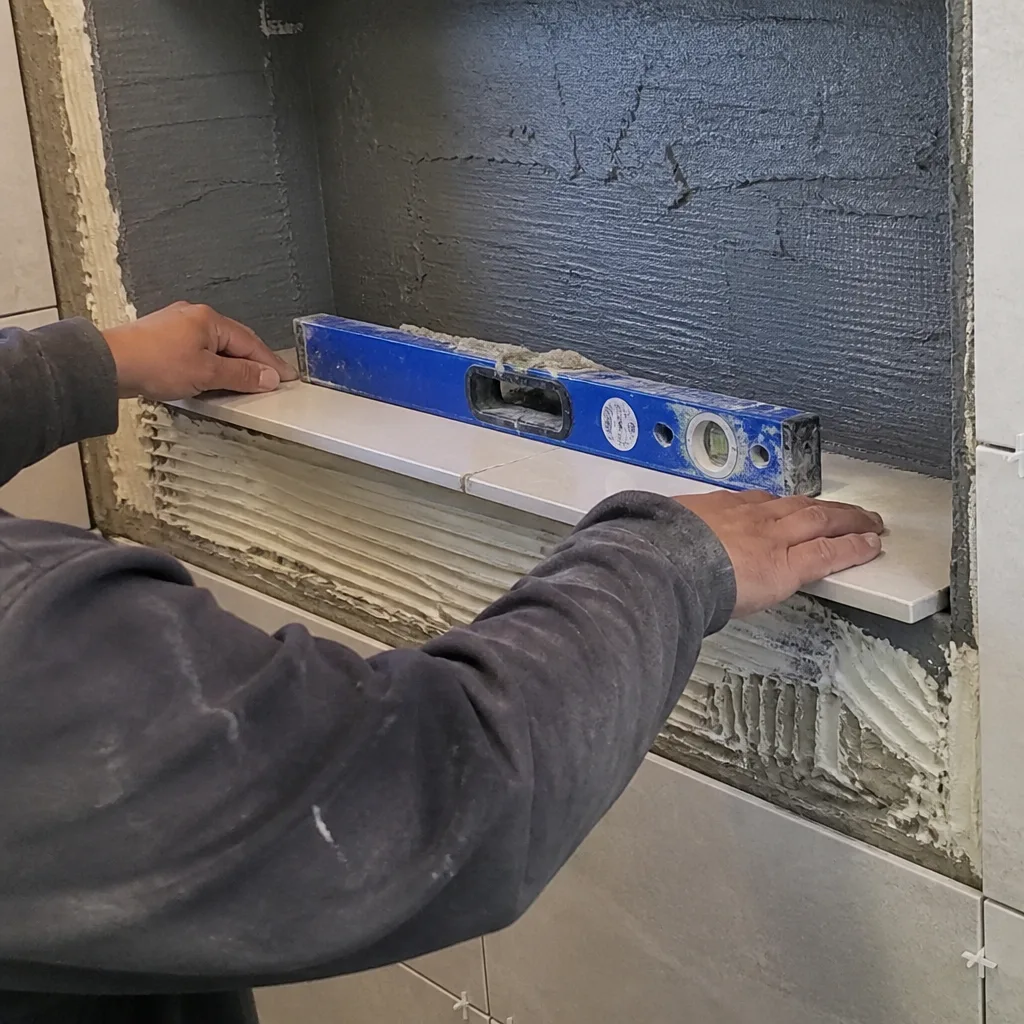 Contractor installing bathroom shower niche tiles with a spirit level.